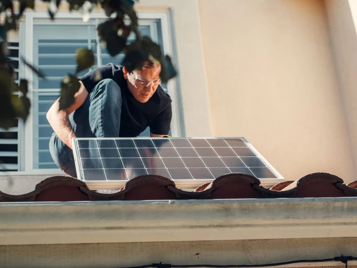 A worker fitting a solar panel on the roof of a house