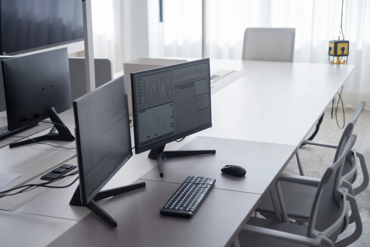 A desk with two monitors showing spreadsheet columns
