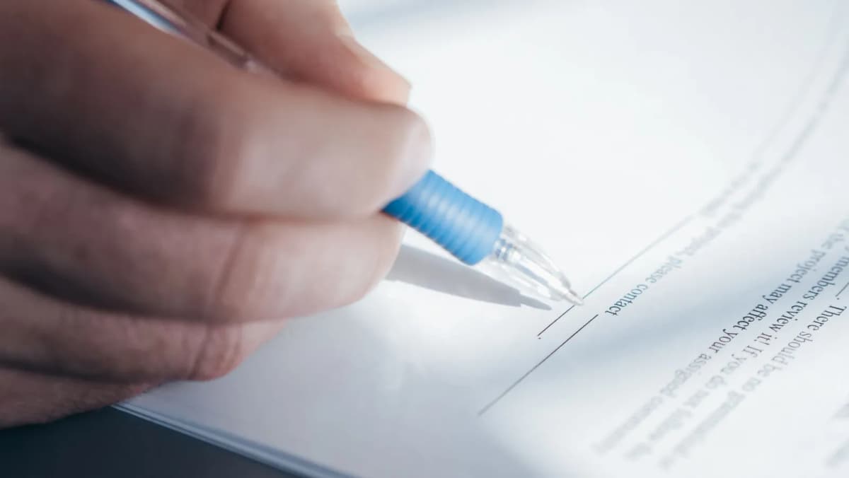 A hand signing a document with a pen