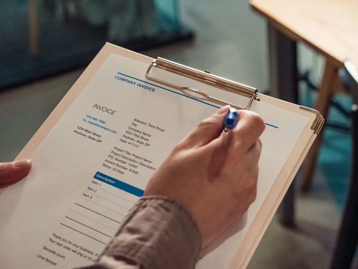A hand holding an invoice on a clipboard with a pen