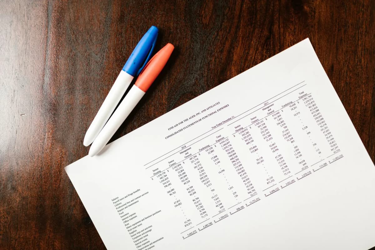 A printed financial statement on a wooden desk with pens