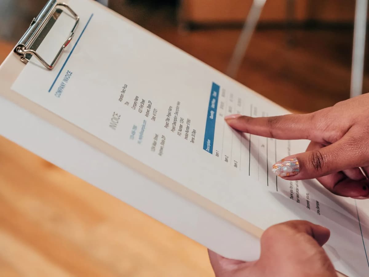 A hand pointing to a line on a printed invoice clipped to a clipboard
