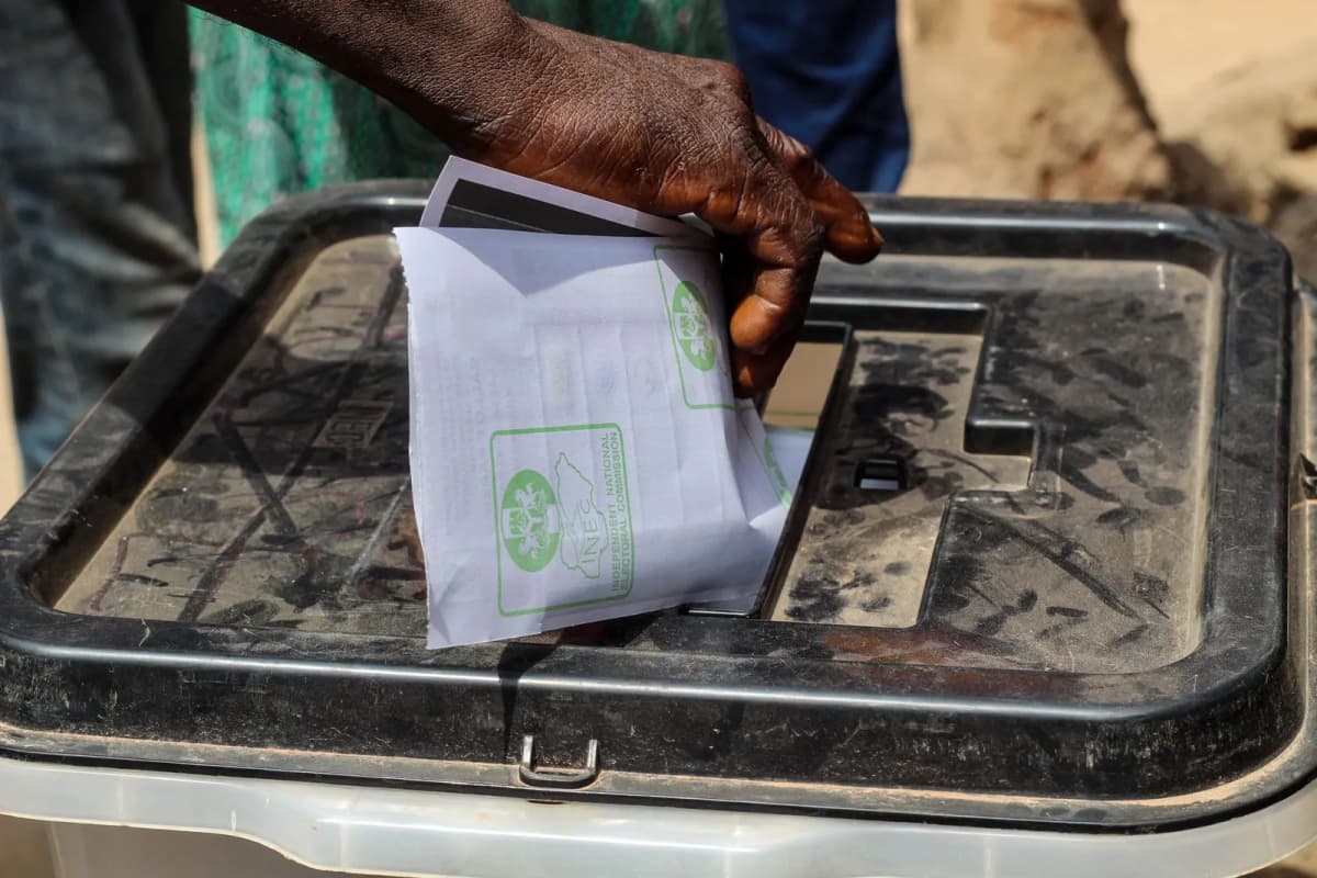 A hand placing a paper ballot into a transparent voting box