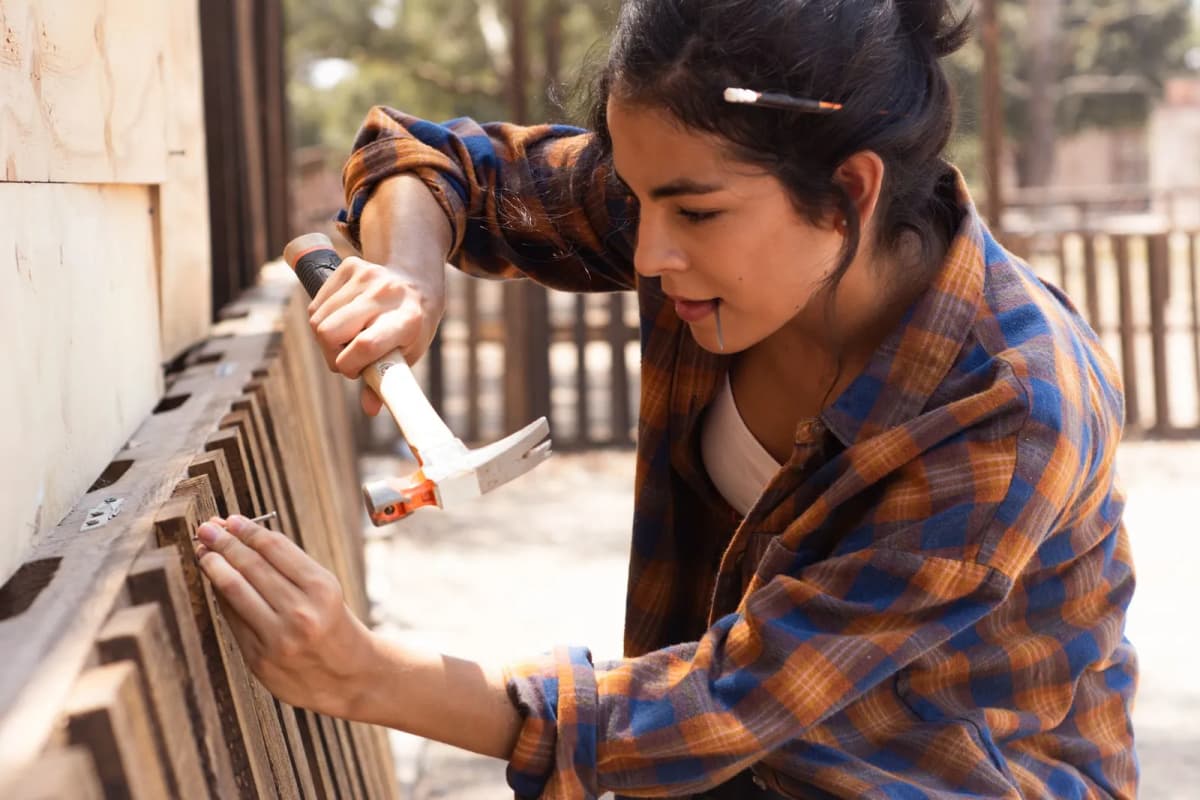 A worker repairing a wooden fence panel with a hammer
