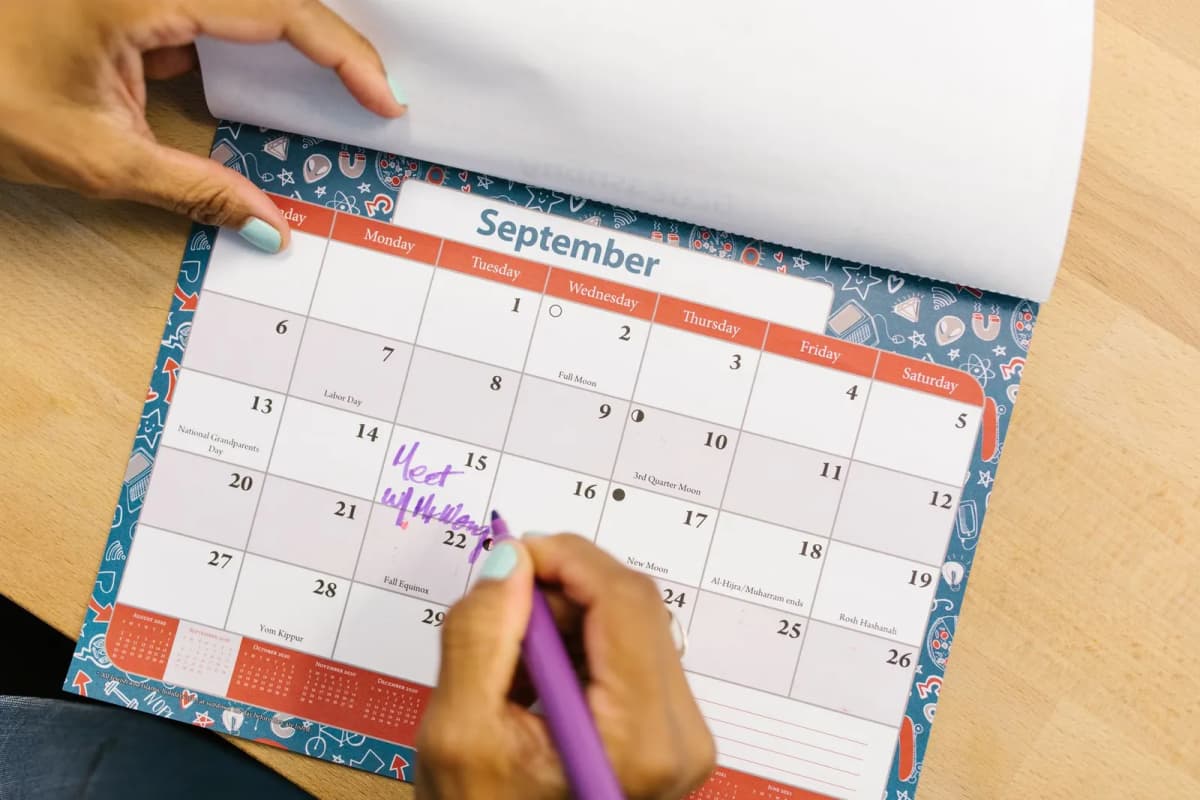 A person marking a September date on a desk calendar with a pen