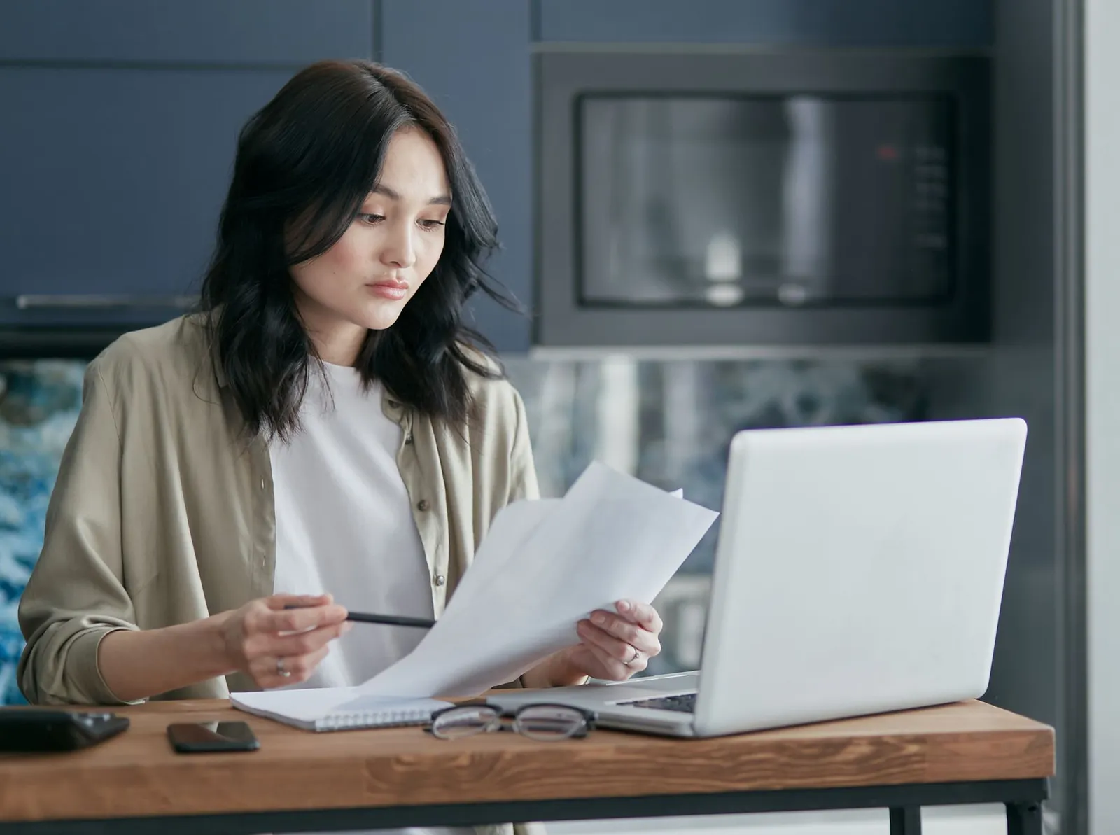 A homeowner reviewing printed documents beside a laptop at a kitchen table