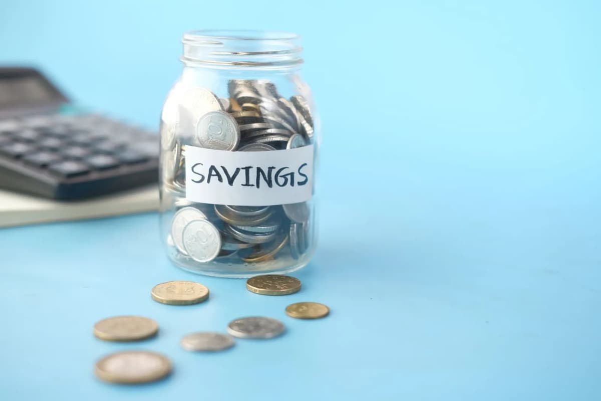 A glass jar labeled savings filled with coins beside a calculator