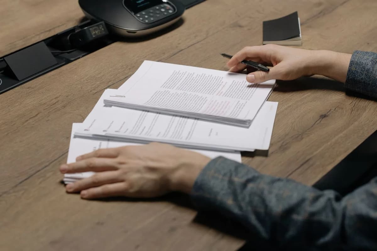 A person reviewing a set of printed documents with a pen at a desk