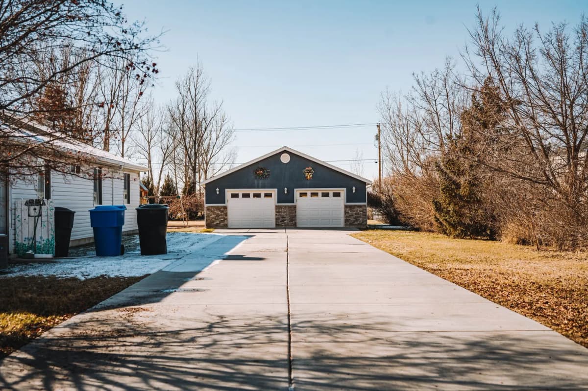 Trash and recycling bins beside a house with a long driveway