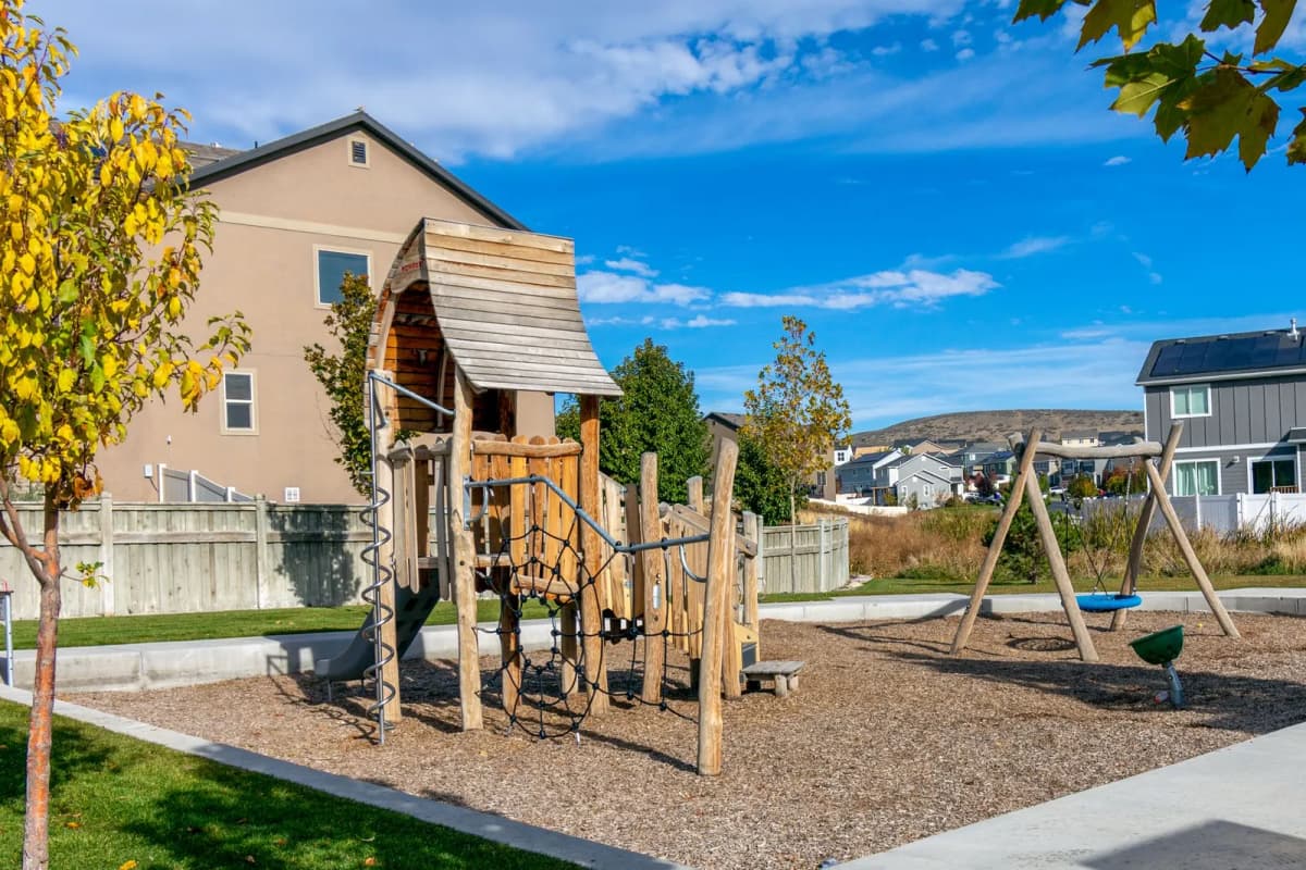 A wooden playground with swings in front of a row of single-family homes
