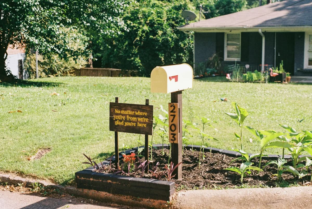 A residential mailbox with a welcome sign and plants in a suburban front yard