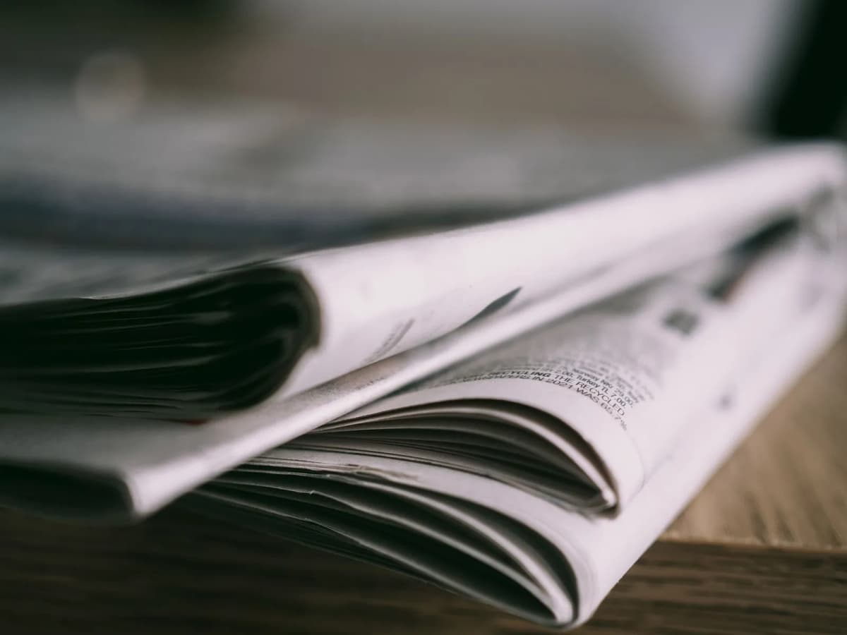 A stack of folded printed newsletters on a wooden table