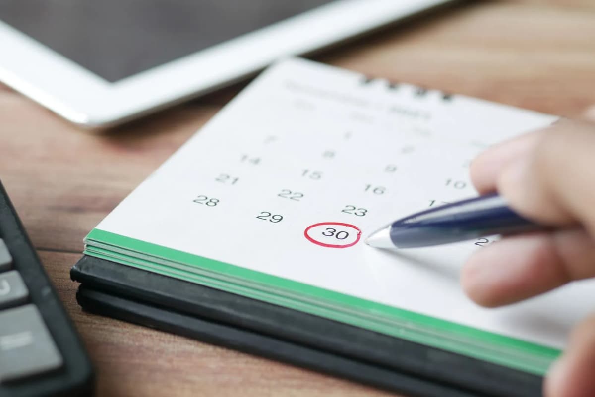 A hand marking a due date on a desk calendar