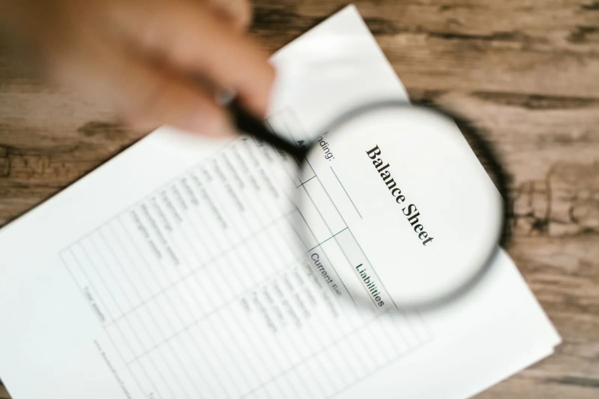 A printed balance sheet under a magnifying glass on a wooden table