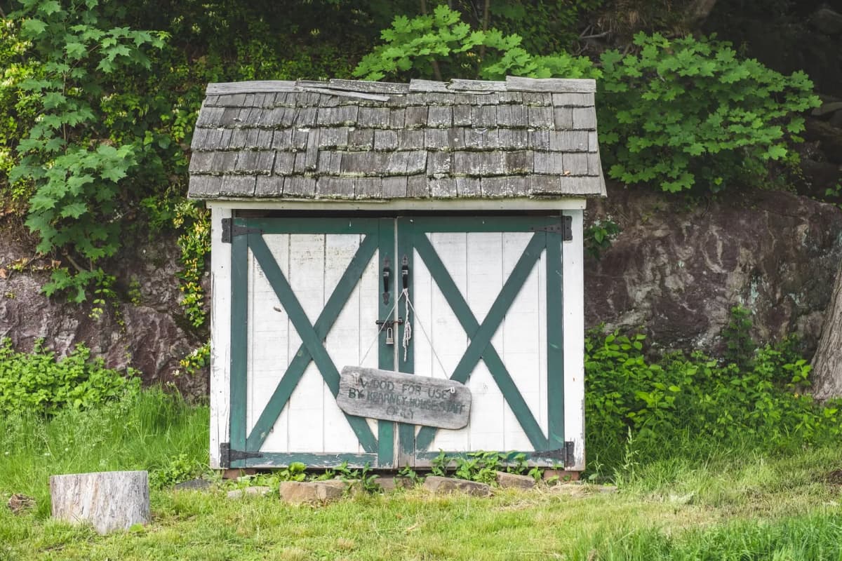 An older wooden storage shed with weathered shingles in a yard