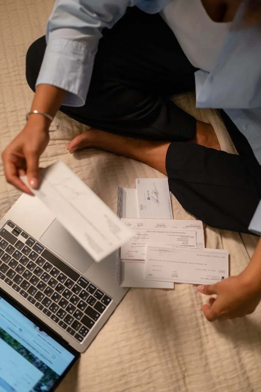 Hands sorting checks beside a laptop