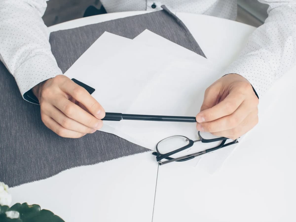 Hands holding a pen over a printed page, with reading glasses on the desk