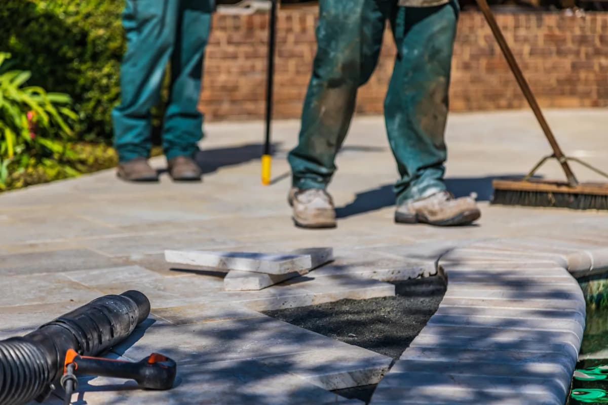 Workers laying stone pavers for a new backyard patio