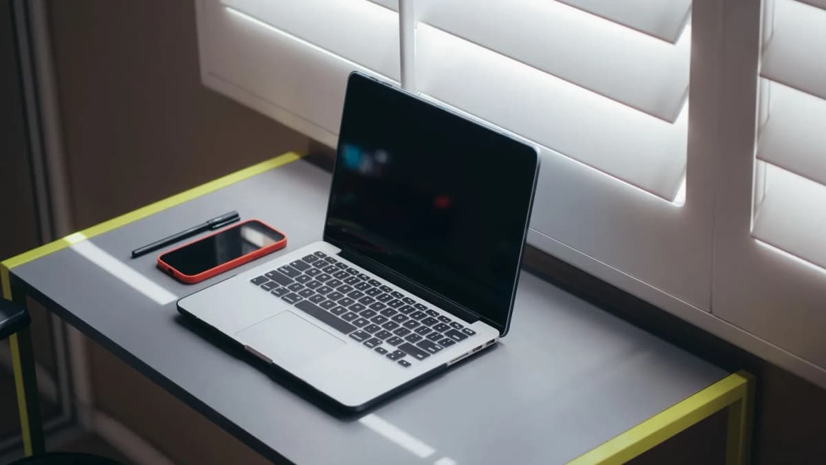 A home desk with a laptop, a smartphone and a pen in natural light