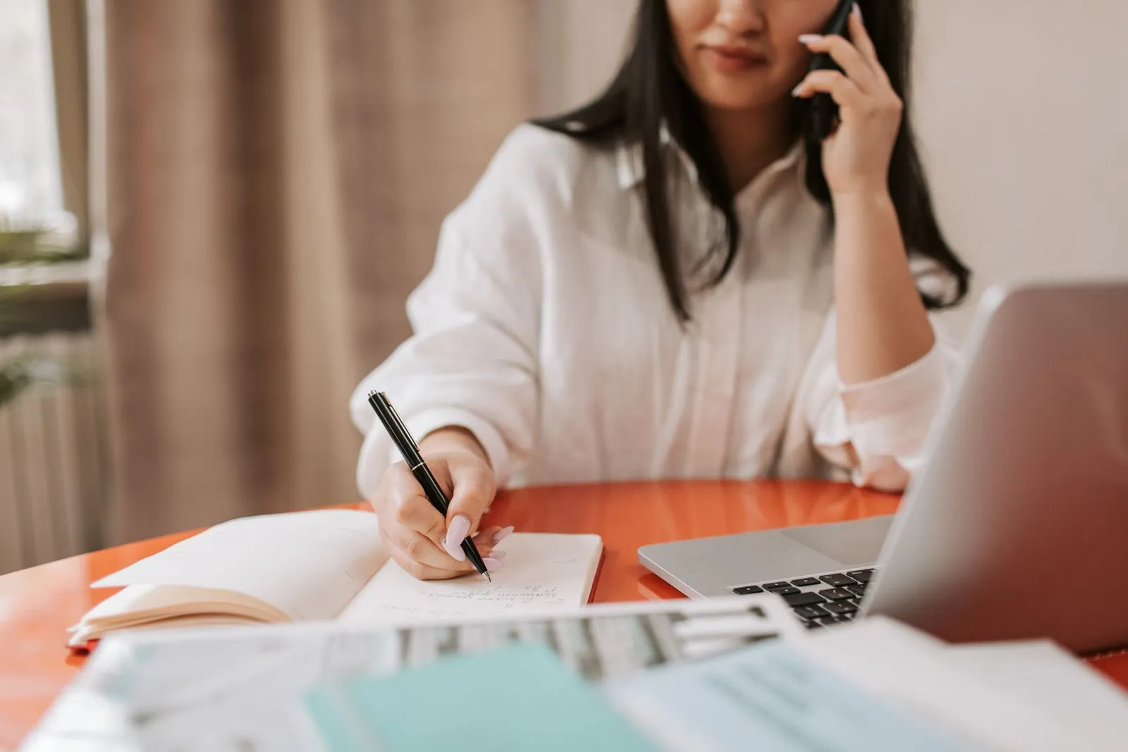 A person taking written notes while on a phone call at a desk