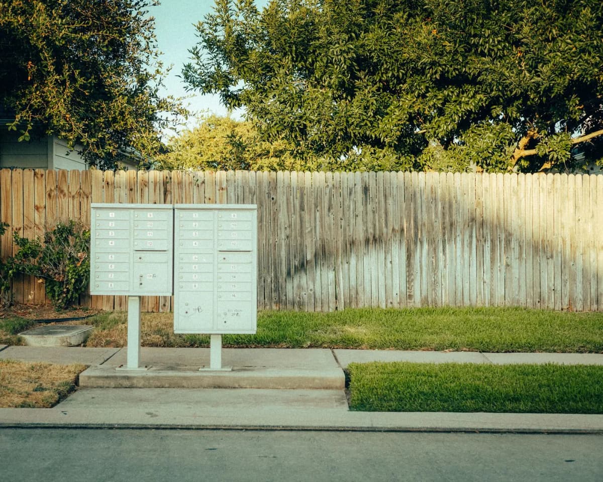 Mailboxes on a suburban street beside a wooden fence and trees