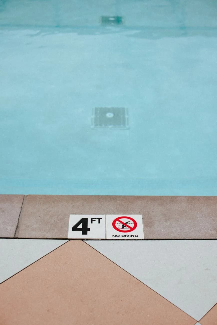 A four-foot depth marker and no-diving symbol on a pool deck beside a floor drain