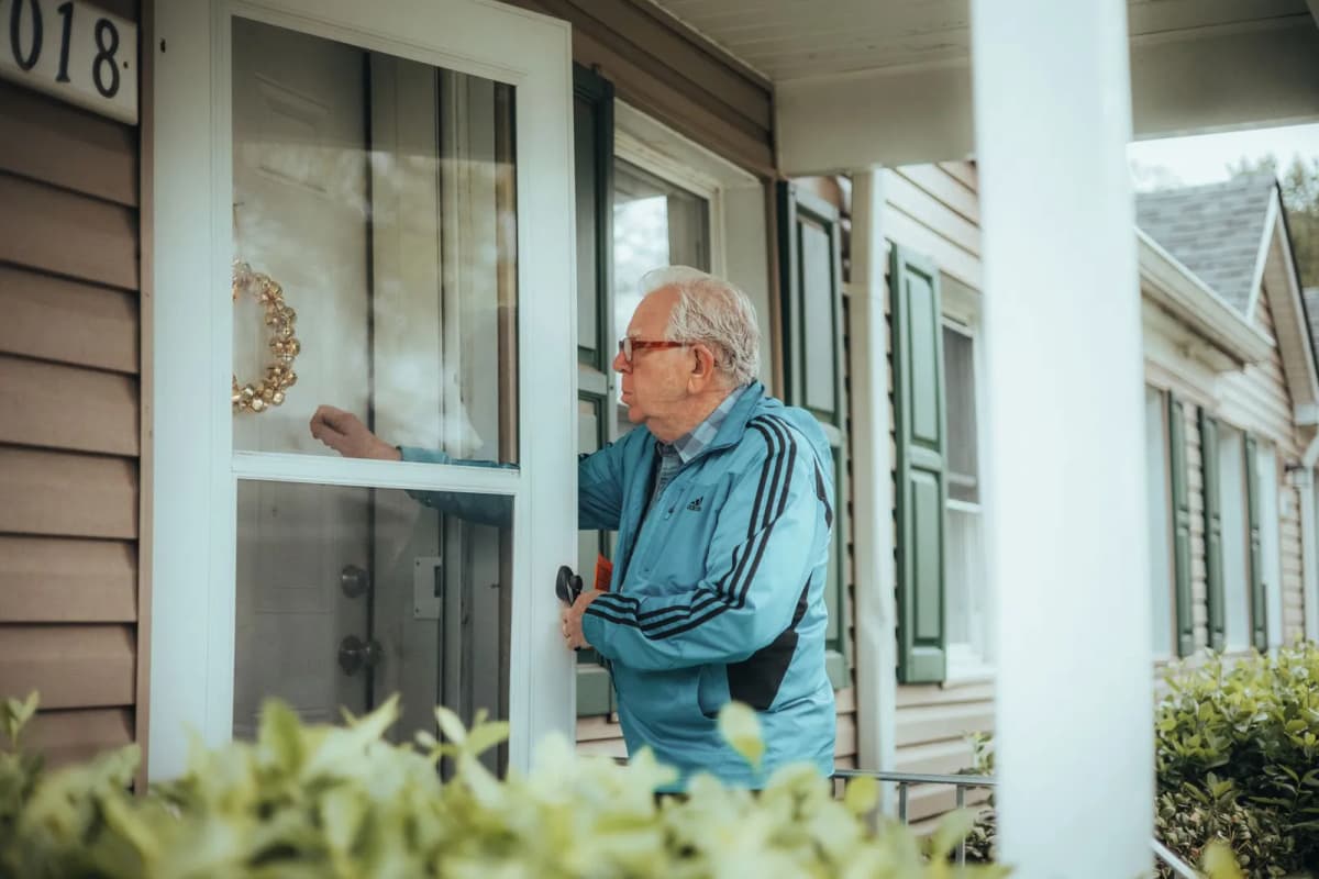An older man knocking on the front door of a suburban house