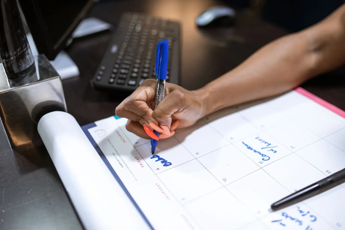 A hand writing a note on a desk calendar with a blue marker