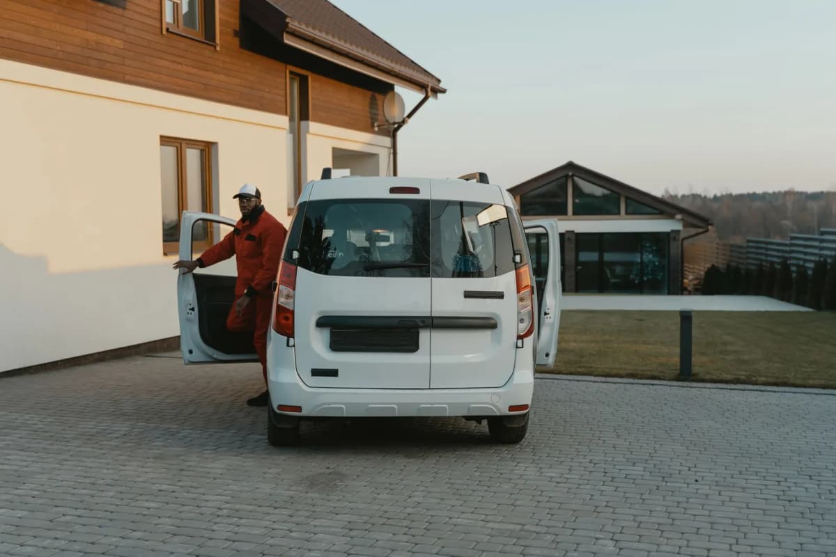 A uniformed worker stepping out of a white service van in a residential driveway