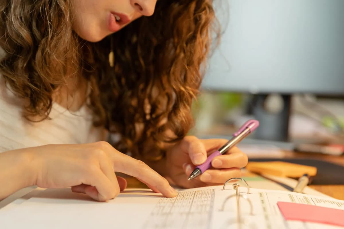 A person marking up the pages of a ring binder with a pen at a desk