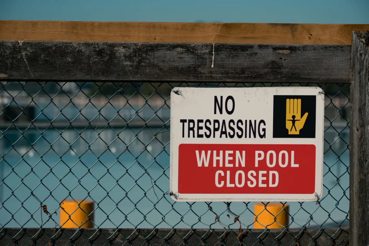 A sign on a chain-link pool fence reading No Trespassing When Pool Closed