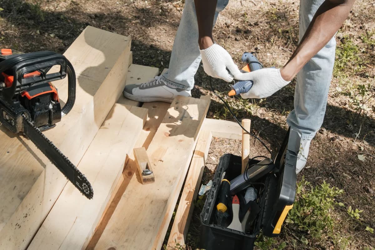 A carpenter working on a wooden panel outdoors with power tools