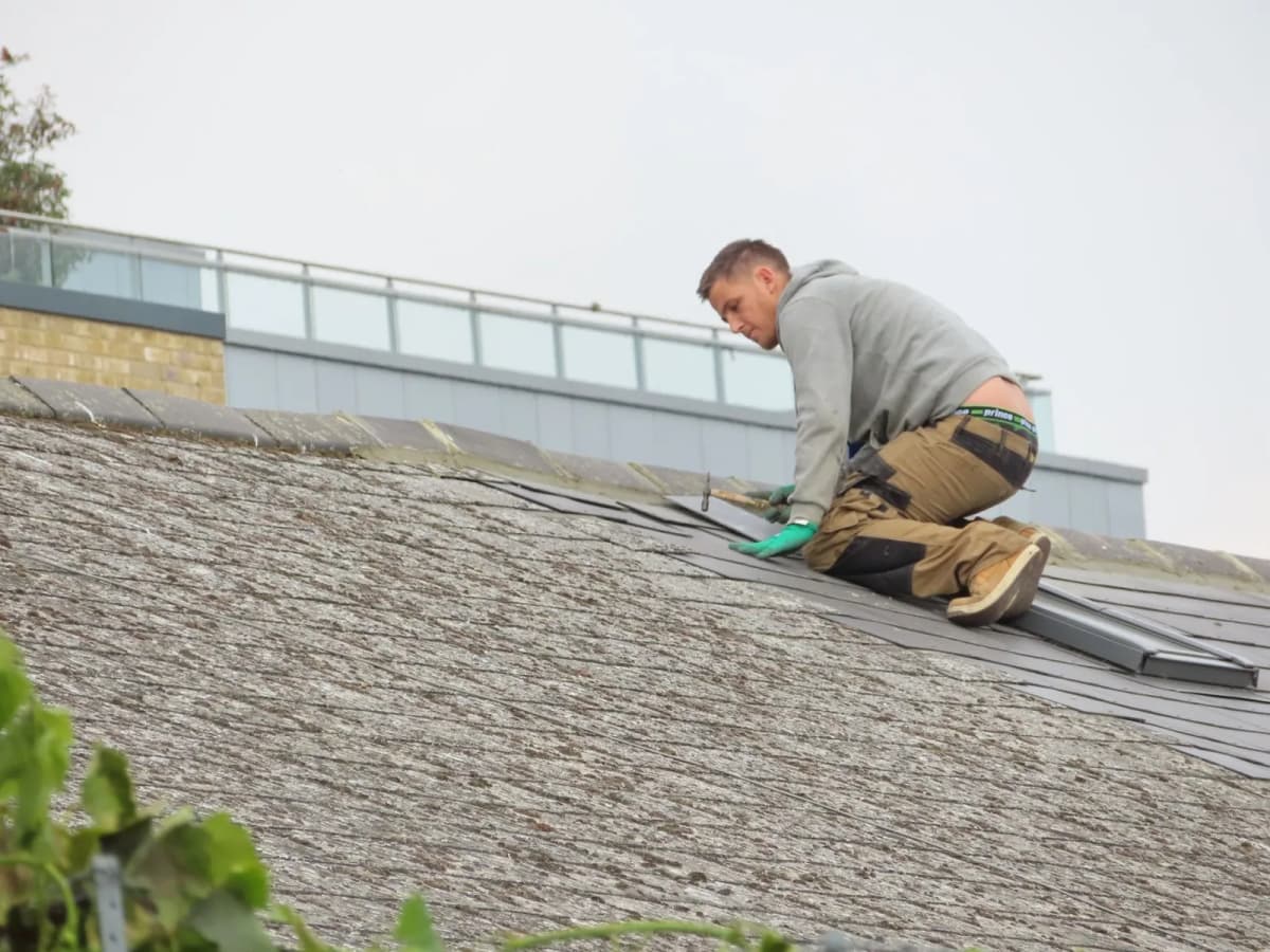 A worker installing shingles on a residential rooftop
