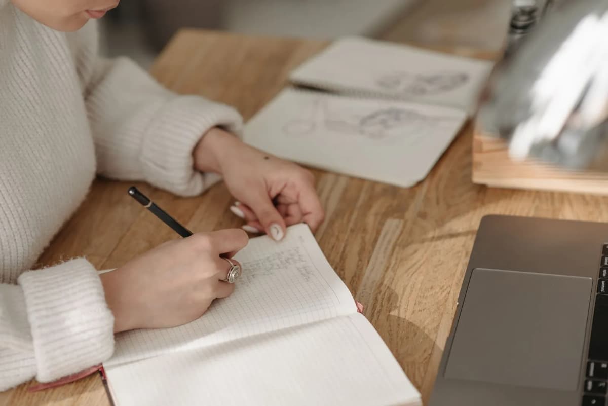 A person writing notes in a lined notebook at a desk