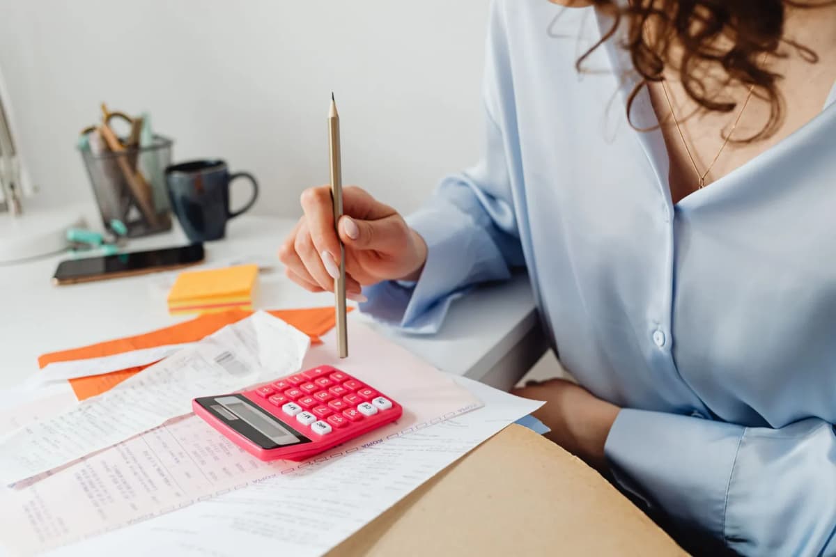 A person at a home desk working through bills and receipts with a calculator and pencil