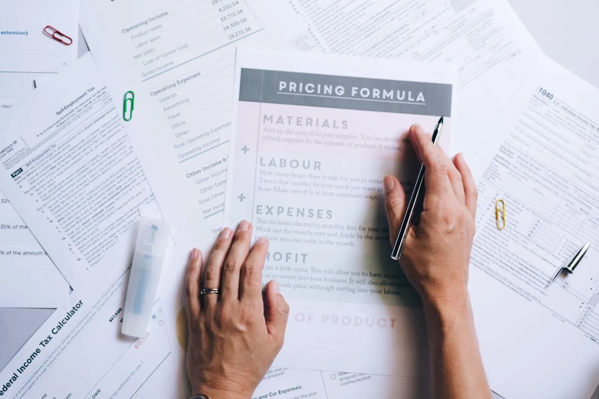Hands sorting through printed financial documents and pricing worksheets on a desk