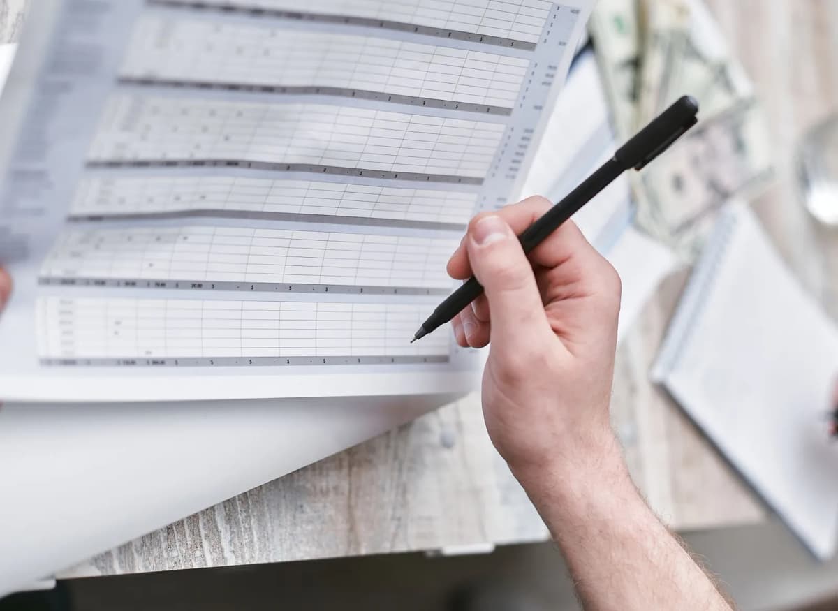 A pen over a printed ledger of figures with cash beside it